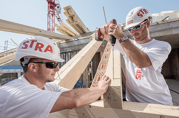 Männer mit Helmen befestigen Bohlen auf einer Baustelle 
