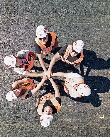 Sechs Personen mit Bauhelmen auf stehen im Kreis und halten ihre Hände in die Mitte.