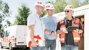 Photo Three men with helmets stand in front of a Strabag car