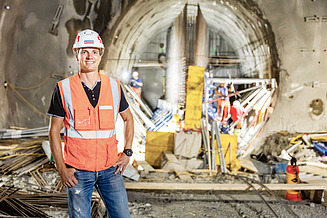 Site manager Florian Fuchs stands on a construction site with a pad and helmet