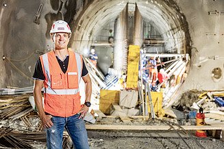 Site manager Florian Fuchs stands on a construction site with a pad and helmet