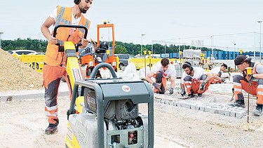 Foto: Ein Lehrling sitzt in der Hocke auf einem Rohbauelement und blickt in die Kamera