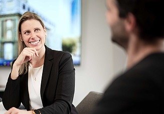 Foto einer Frau im Büro, die einem Kollegen interessiert zuhört
