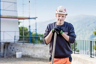 Foto: Ein Lehrling stützt sich auf eine Schaufel und blickt in die Kamera