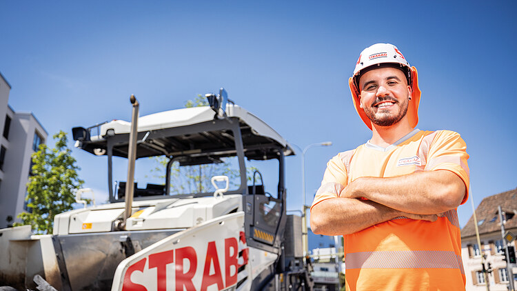 Ein Polier im Strassenbau steht mit verschränkten Armen vor einem Asphaltfertiger