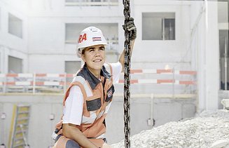 Foto Frau mit Helm hockt auf Baustelle und hält sich an Kette fest