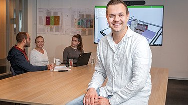 Vier Männer in einem Baucontainer betrachten einen Plan auf dem Tisch