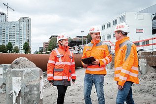 Zwei Bauarbeiter mit Helm betrachten ein aufgestelltes Messgerät (Zwei Bauarbeiter mit Helm betrachten ein aufgestelltes Messgerät)