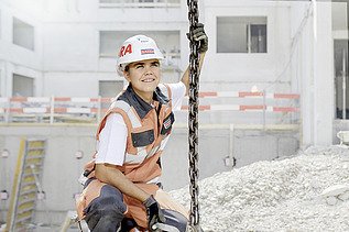 Foto Frau mit Helm hockt auf Baustelle und hält sich an Kette fest