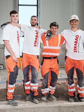 Three apprentices standing in workwear in front of excavators