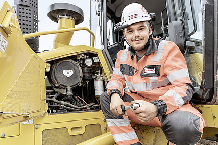 Praktikant gleda u kameru, iza njega je radni stroj