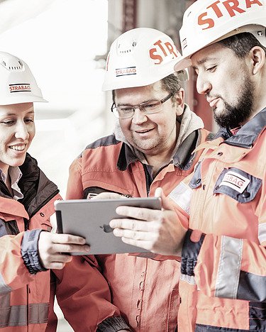 Unser Versprechen Menschen mit STRABAG-Helmen auf der Baustelle stehen zusammen