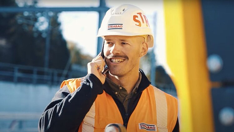 Porträt eines Mannes mit Bauhelm und Schutzweste am Mobiltelefon