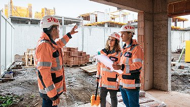 Karriere Bild 3 3 Bauarbeiter:innen mit Arbeitskleidung und Helm auf einer Baustelle