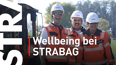 Drei STRABAG-Mitarbeiter in Arbeitskleidung stehen vor einem Bagger und lächeln in die Kamera. Im Vordergrund steht in weißer Schrift 