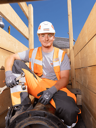 Fiatal férfi építőipari sisakban, fémcsövön ülve