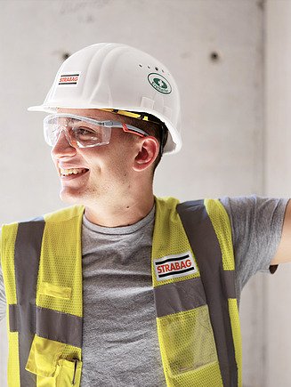 Foto werknemer met high-visibility vest, bouwhelm en veiligheidsbril kijkt opzij