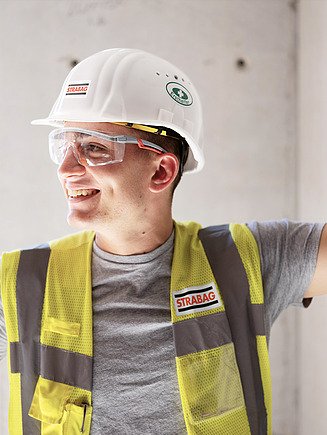 Slika zaposlenog koji nosi zaštitni prsluk, kacigu i zaštitne naočare gleda u stranu