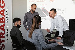 Fotografija četvero ljudi u uredu, jedan muškarac sjedi na stolu