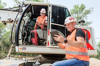 Kolega pokazuje na tabletu drugom kolegi koji sjedi u bageru