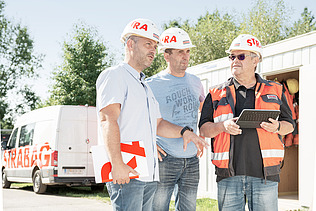 Foto Tři muži s helmami stojí před vozem Strabag