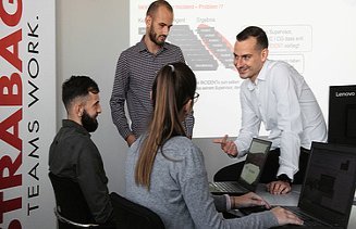 Fotografija štirih ljudi v pisarni, en človek sedi na mizi