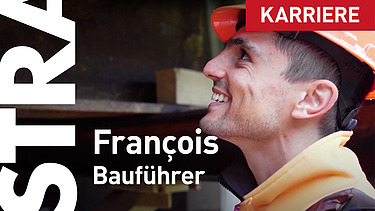 Ein STRABAG-Bauführer lächelt auf seiner Baustelle bei der Arbeit. Er trägt einen Orangenhelm und im Hintergrund kann man Stahlträger verschwommen erkennen. 