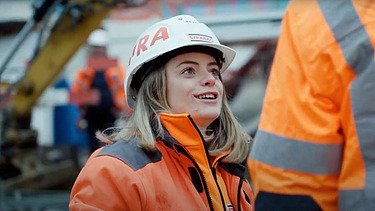 Juniorbauführerin in oranger Arbeitskleidung mit Helm