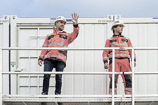 Photo Two men standing by the container left man raised hand