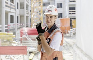 Foto Frau mit Helm auf Baustelle zieht Handschuhe an