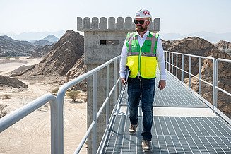 Site manager Florian Fuchs stands on a construction site with a pad and helmet