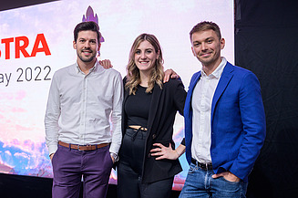 Das adASTRA-Kernteam, bestehend aus Franz, Joy-Estelle und Pawel, stehen auf der einer Bühne