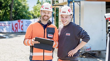 Foto Zwei Bauarbeiter mit weißen Helmen blicken in die Kamera