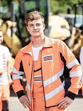 Three apprentices standing in workwear in front of excavators