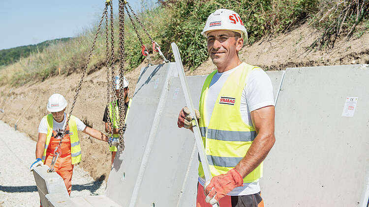 Un bărbat stă pe șantier și zâmbește către cameră.