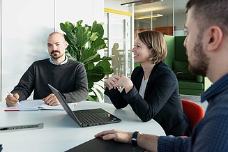 Drei STRABAG-Mitarbeiter:innen sitzen zusammen an einem Tisch mit Laptops