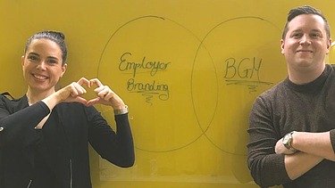 Two employees stand in front of a blackboard 