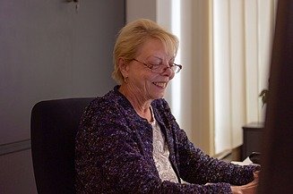 Egy nő ül az asztalnál és mosolyog munka közben