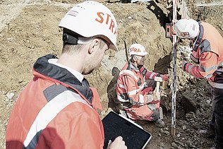 Photo Three men on construction site two survey one noted