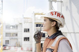 Foto Frau mit Helm auf Baustelle führt Funkspruch durch