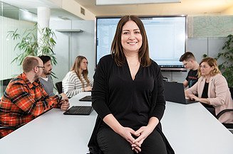 Woman sitting on a table and smiling to the camera.