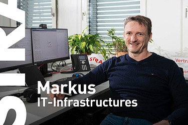Mann sitzt im Büro vor seinem Arbeitsplatz und blickt in die Kamera
