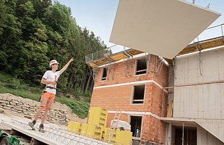Foto: Ein Bauarbeiter dirigiert eine am Kran hängende Betonplatte.