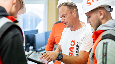 A foreman explains something to his team on a tablet