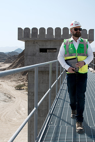 Site manager Florian Fuchs stands on a construction site with a pad and helmet