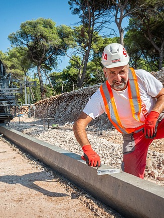 Slika muškarca s kacigom na gradilištu kako radi rubnjak