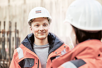 Das Traineeprogramm in der Praxis Foto Mitarbeiter mit Bauhelm blickt Mitarbeiterin mit Bauhelm an