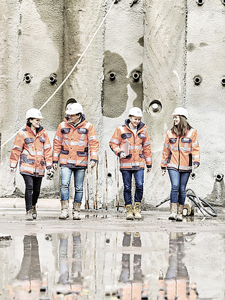 Zdjęcie Czterech pracowników w odzieży ochronnej przed betonową ścianą
