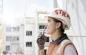 Foto Frau mit Helm auf Baustelle führt Funkspruch durch