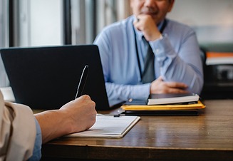 Person macht sich Notizen bei einem Gespräch mit einer anderen Person im Büro.